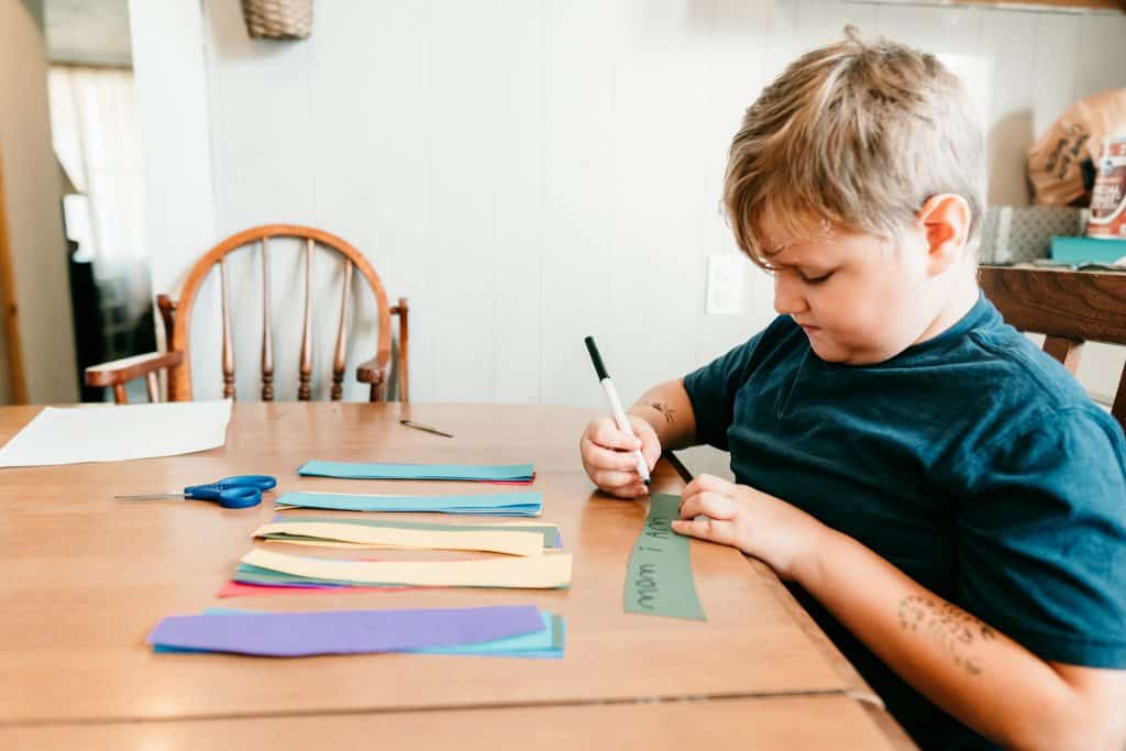 Boy writing what he's thankful for on paper to make a thankfulness paper chain.