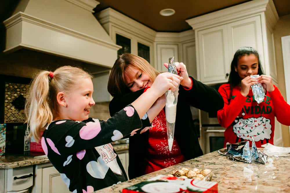 Woman helping girl with icing to decorate gingerbread houses