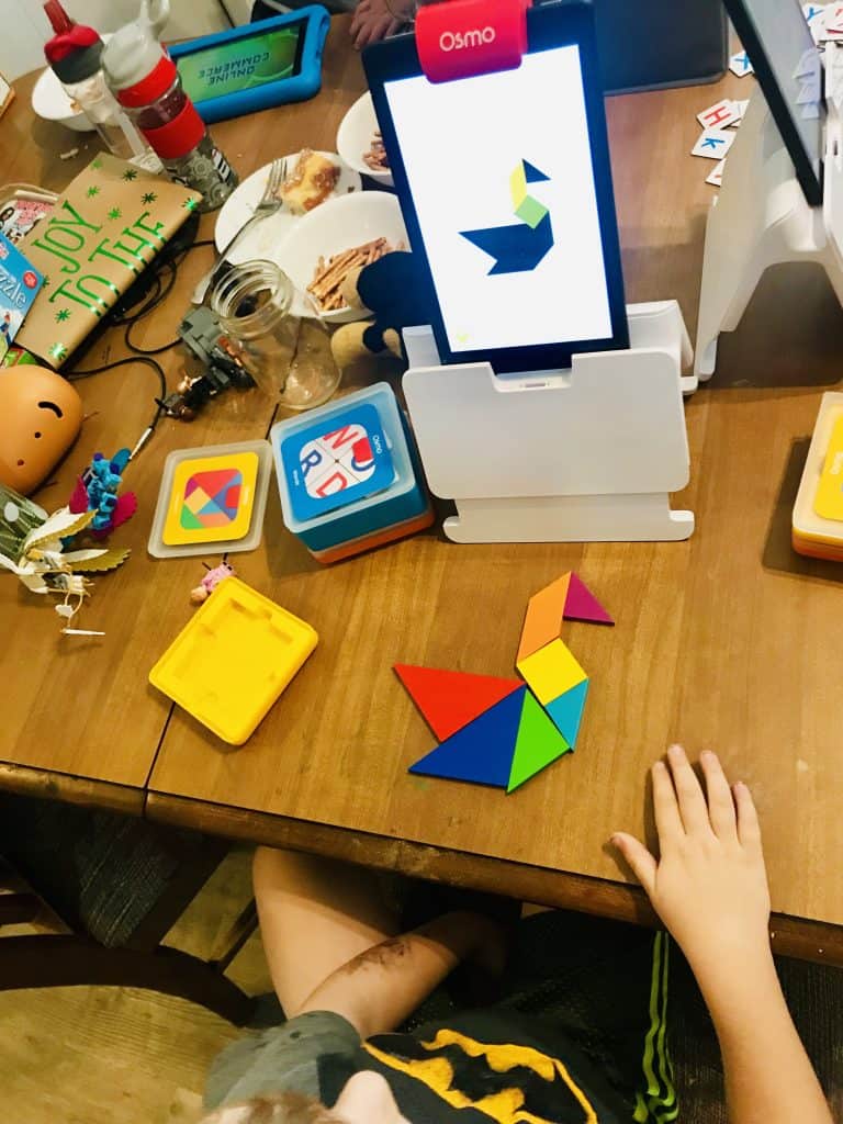 Boy playing Tangram Osmo Game on a Kindle Fire on a messy table.