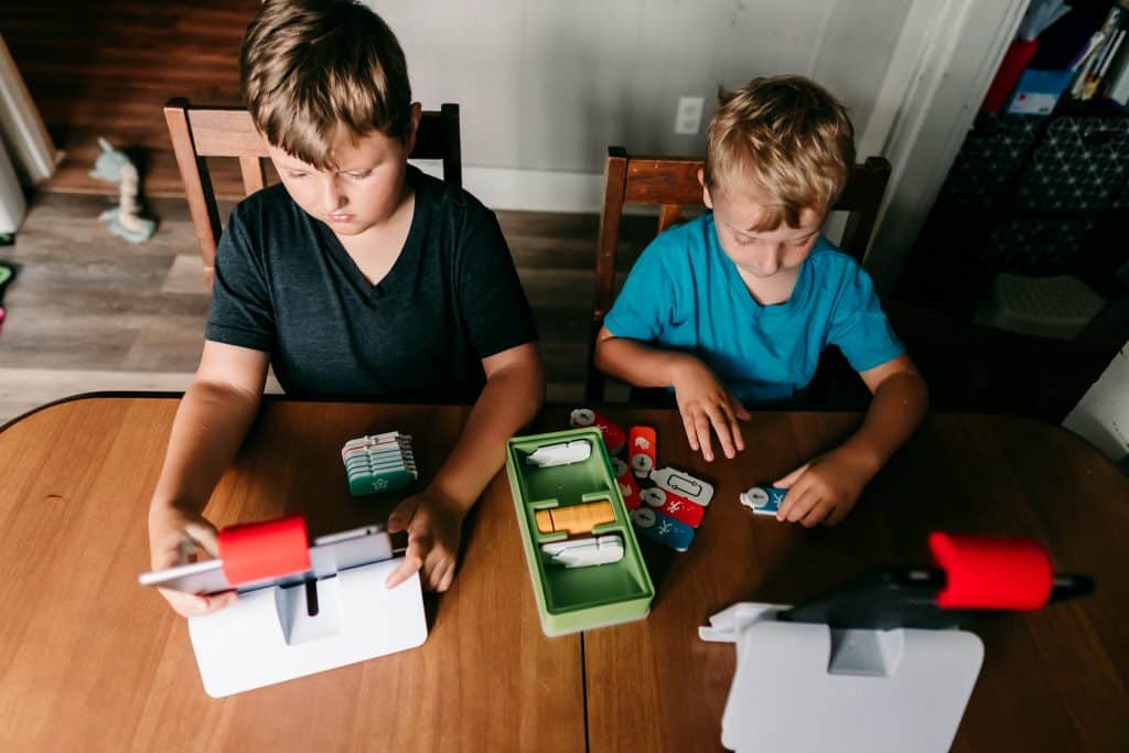 Two boys playing Osmo Coding Games at a kitchen table with hands-on game pieces and tablets on stands.