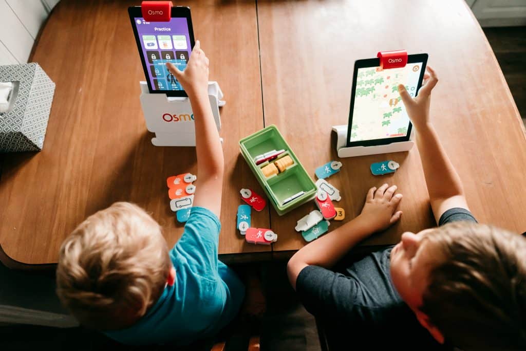 Two boys playing Osmo Coding games with hands-on game pieces at a kitchen table.