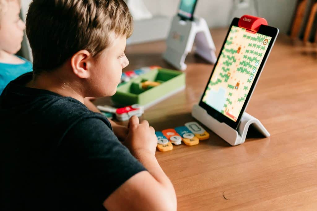 Boy playing Osmo Game Coding Awbie with hands-on game pieces and an iPad on stand.