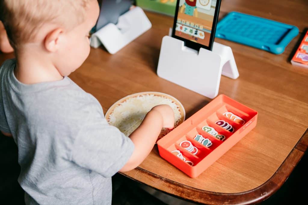 Three year old boy playing Osmo Pizza Co game with game pieces and kindle fire tablet