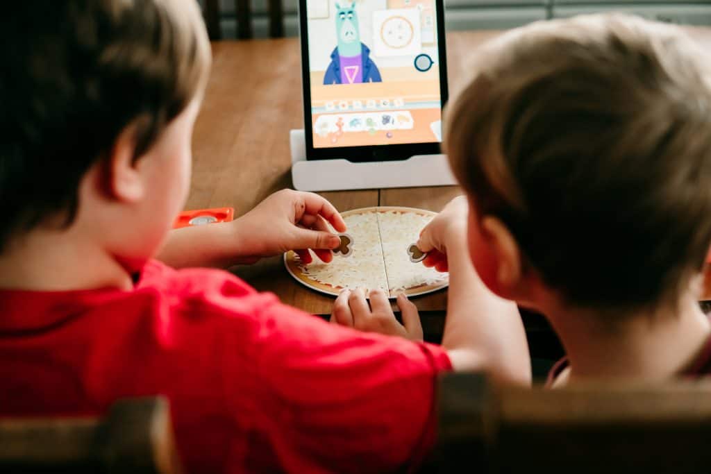 Two boys playing Osmo Pizza Co game on an iPad with hands-on game pieces.